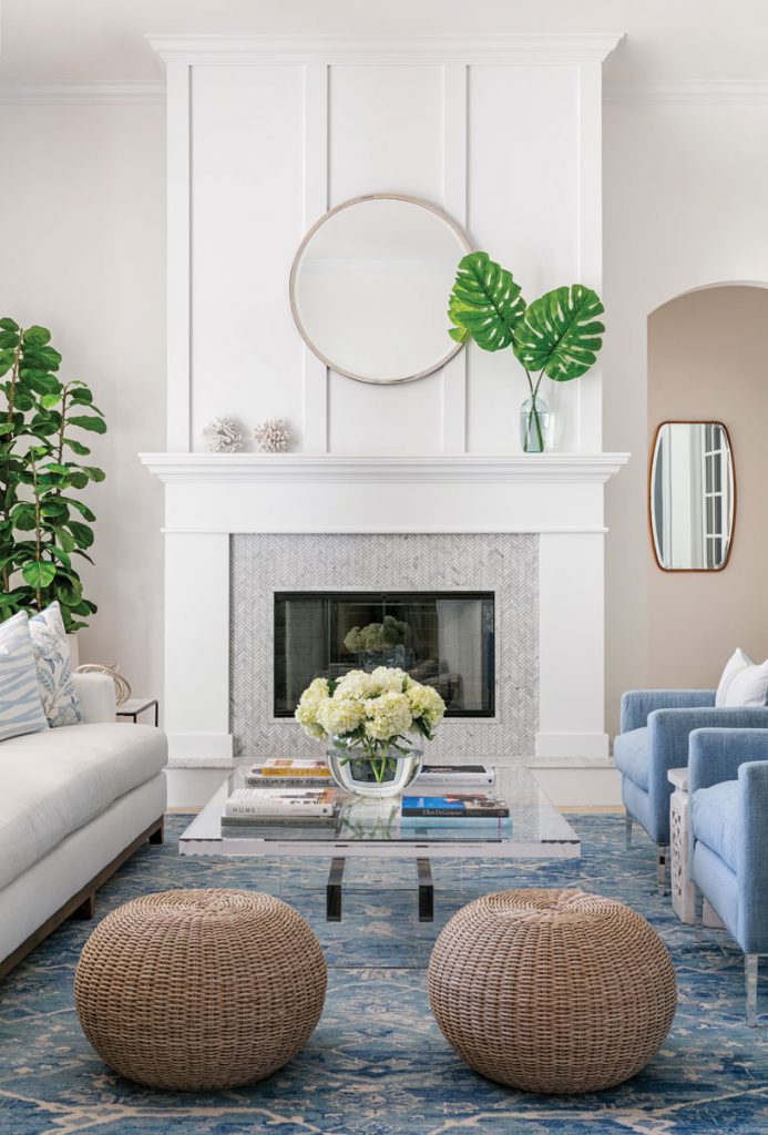 Earth and water tones paired with the natural material of the rattan ottomans set the tone for biophilic design in this living room, while bringing in plants and flowers heightens the look. Photo Credit Sargent Photography